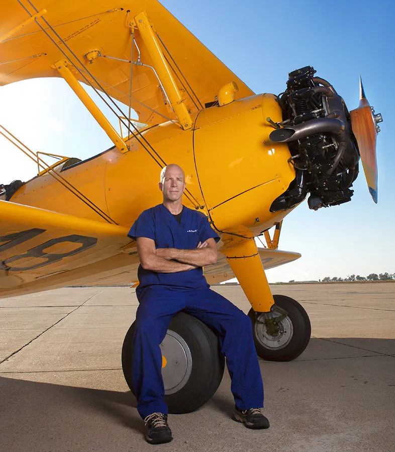 Dr. Ian Purcell beside a yellow biplane on an airfield